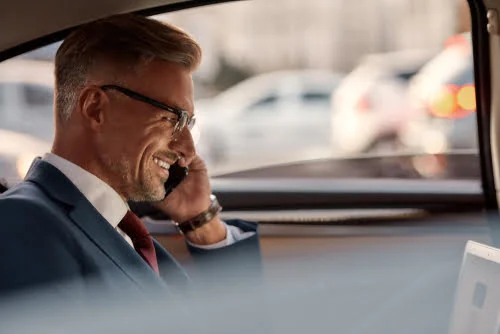 So happy to use airport car service. Side view of mature businessman sitting in the car and talking by the phone